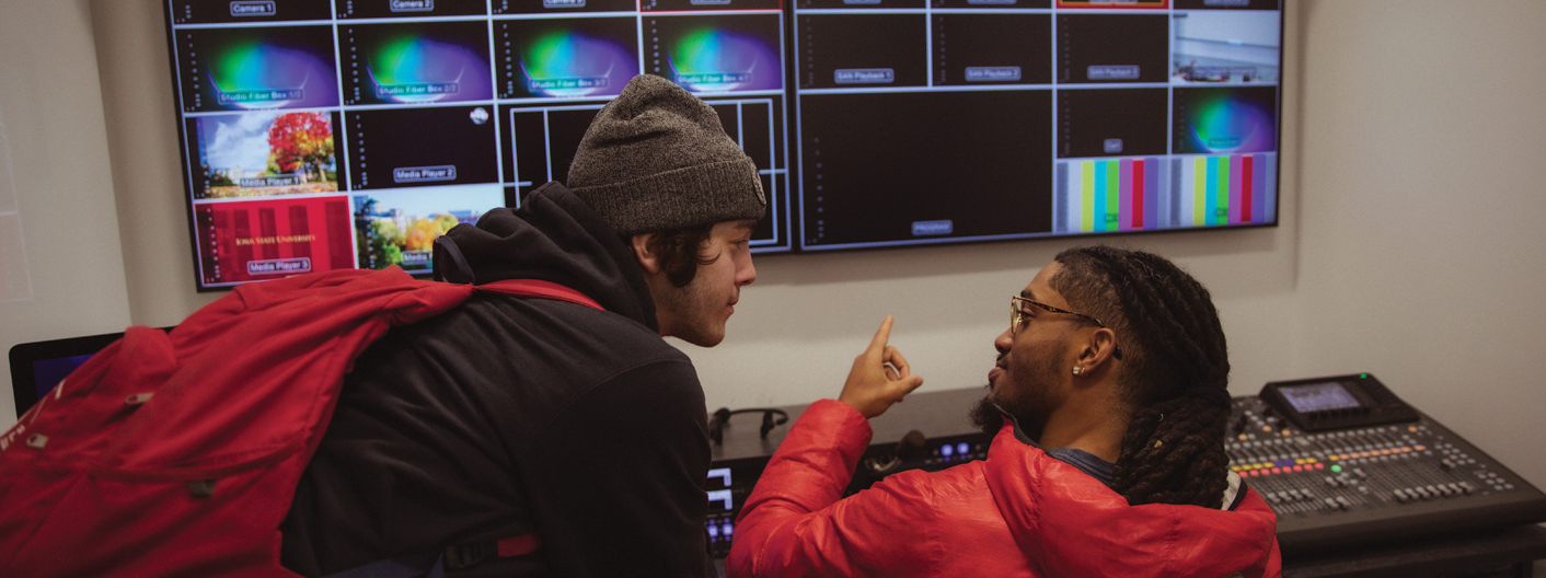 two students in front of many monitors in a multimedia lab