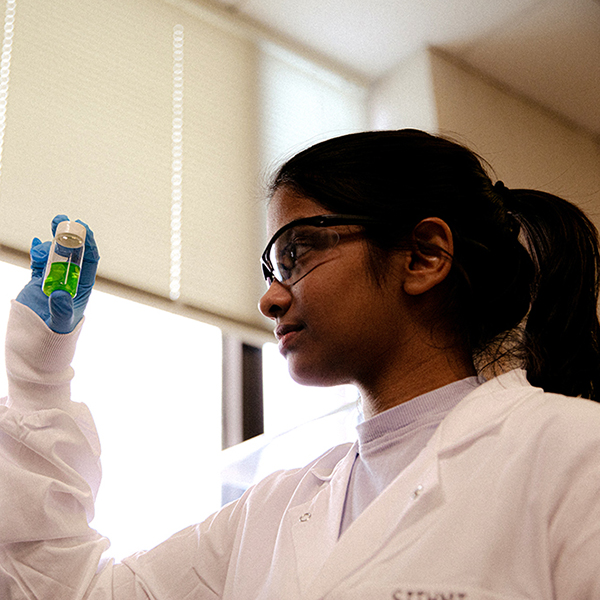 Student conducting undergraduate research holds a small jar of liquid to examine its contents